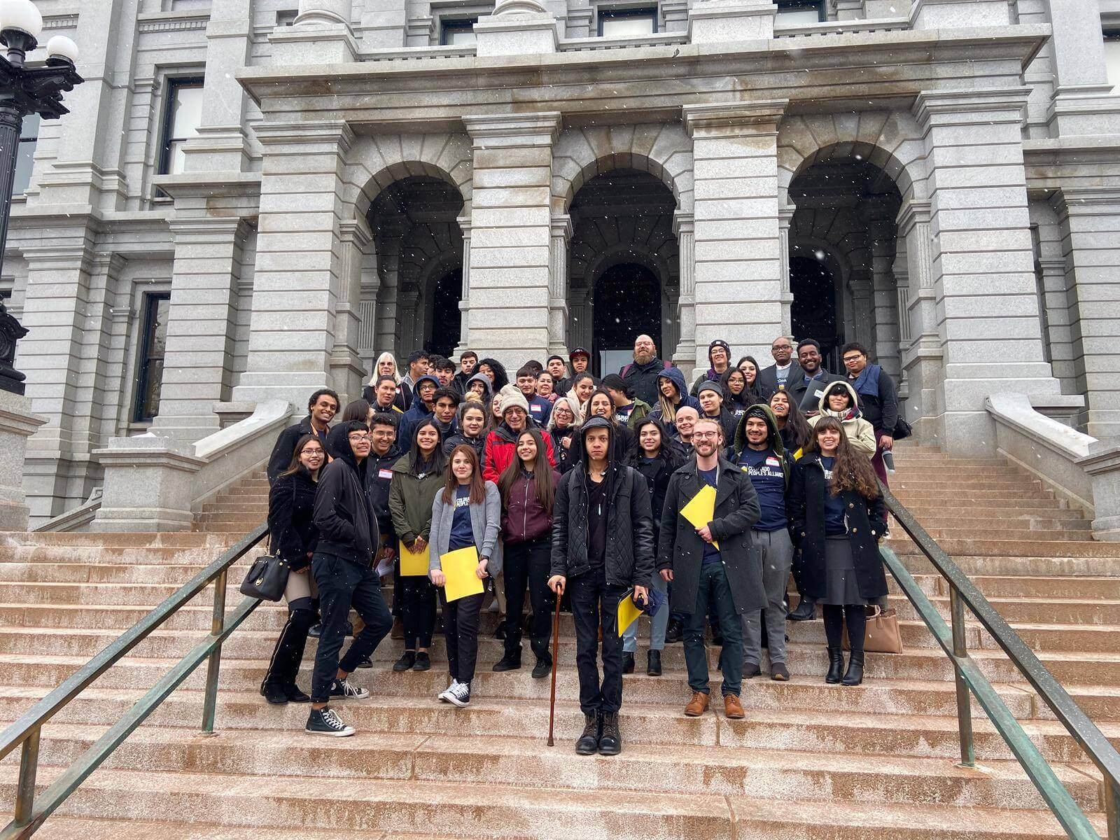 A large group stands on the steps of the Colorado state capitol building
