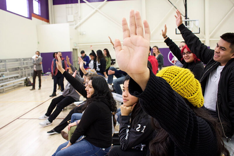 Students in a gymnasium raising their hands