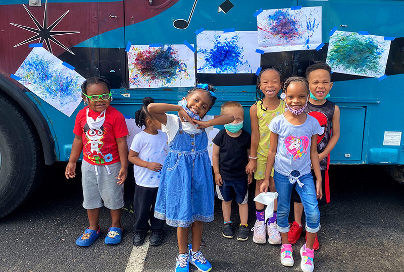 Young students of color pose in front of their abstract artwork