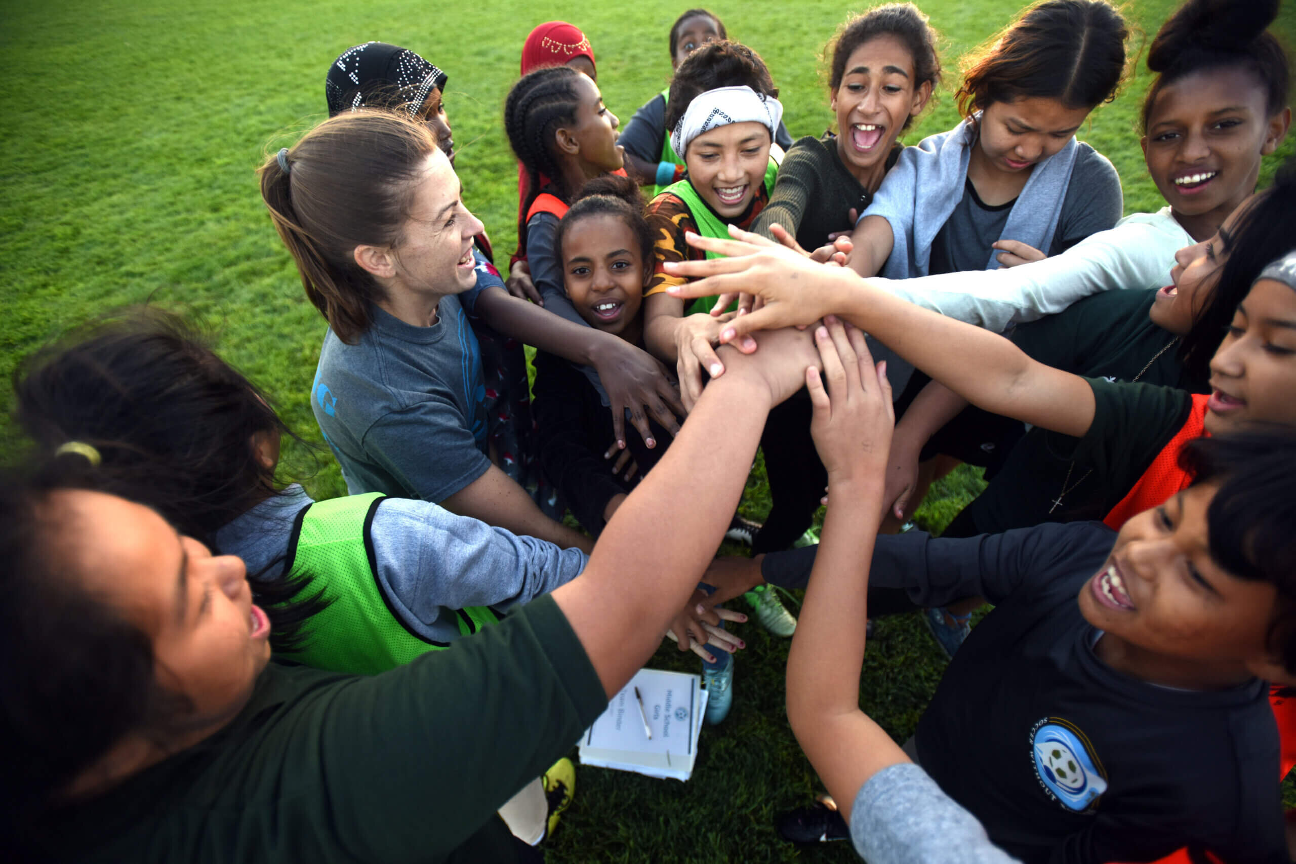 A group of young soccer players from Soccer Without Borders puts their hands in a circle