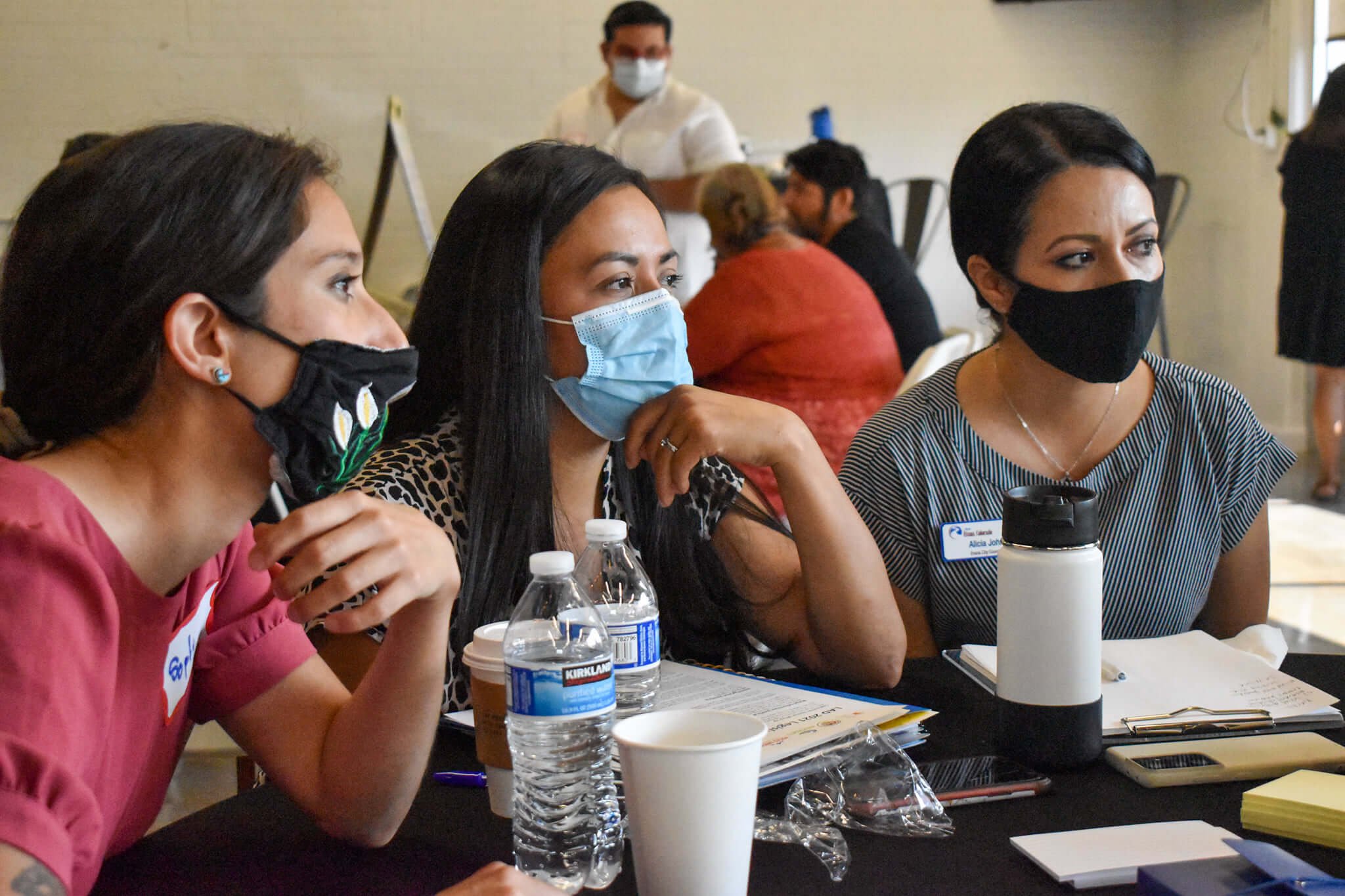 Three women of color with masks on having a discussion around a table