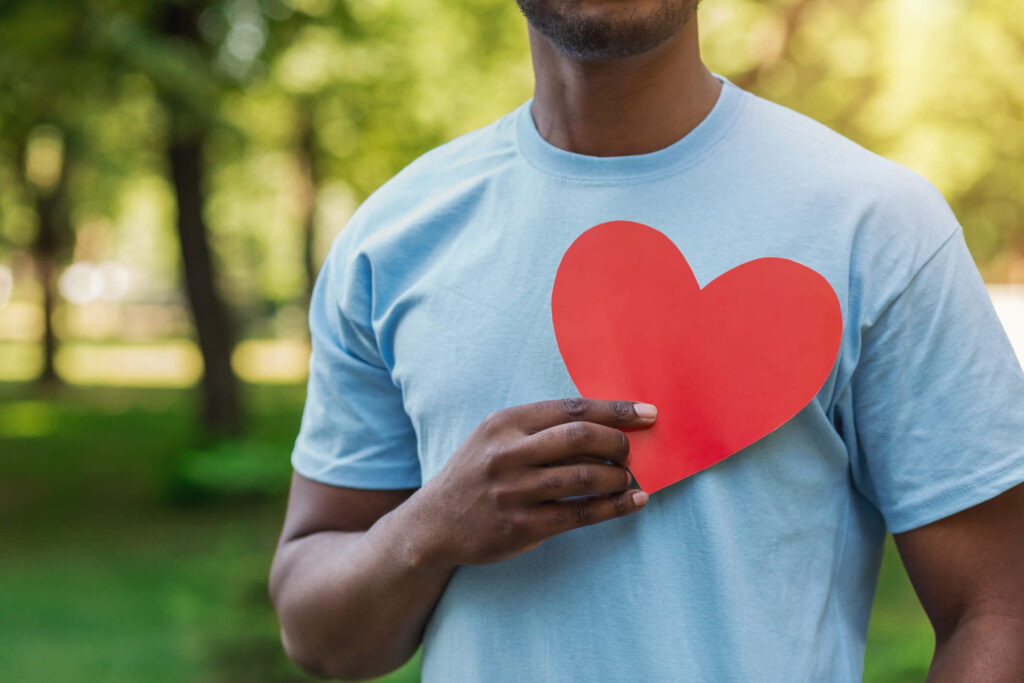 A man of color holds a cutout paper heart over his chest