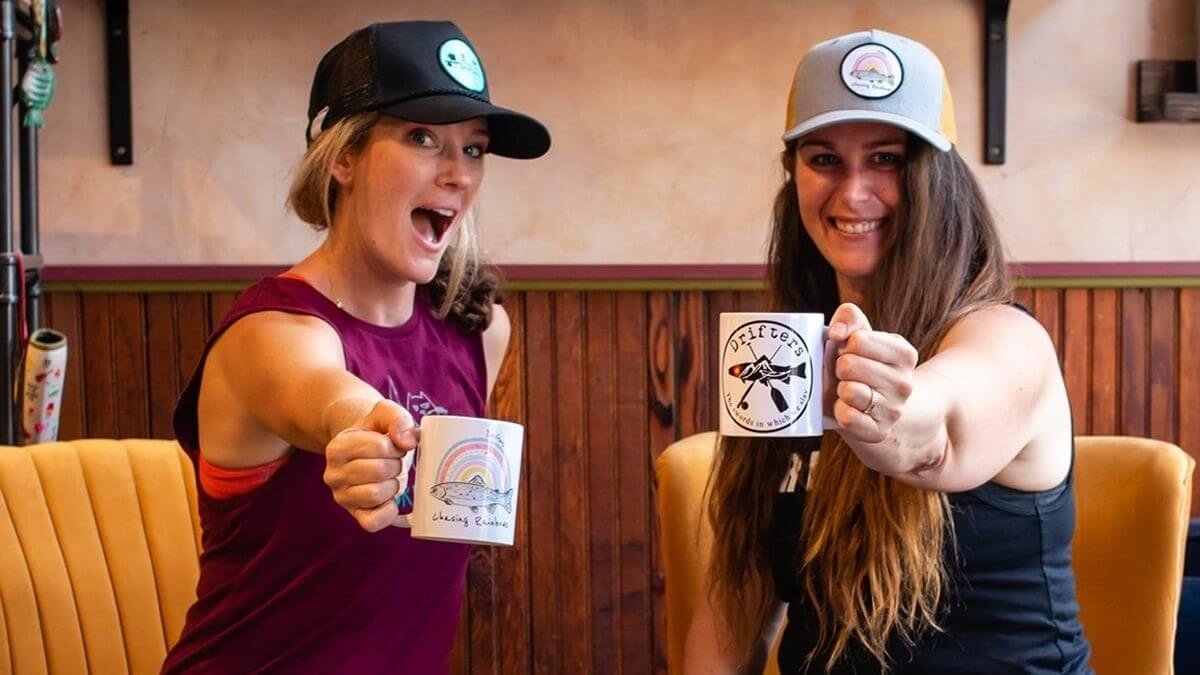 Two women holding mugs to the camera pose for a photo
