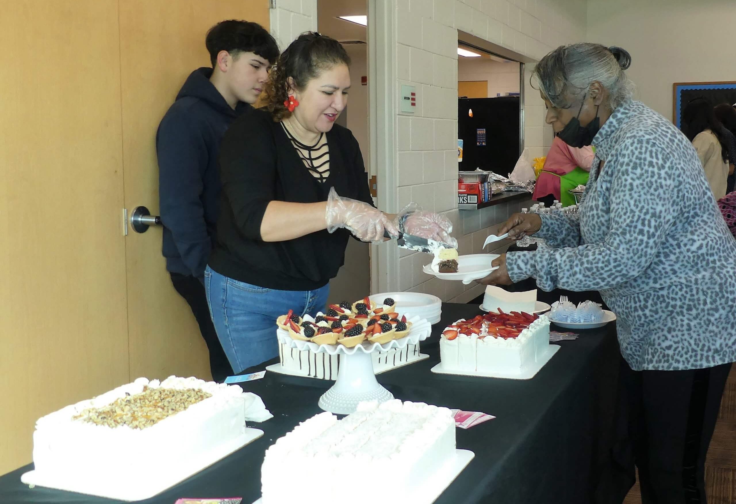 A woman serves cake to another woman at a potluck