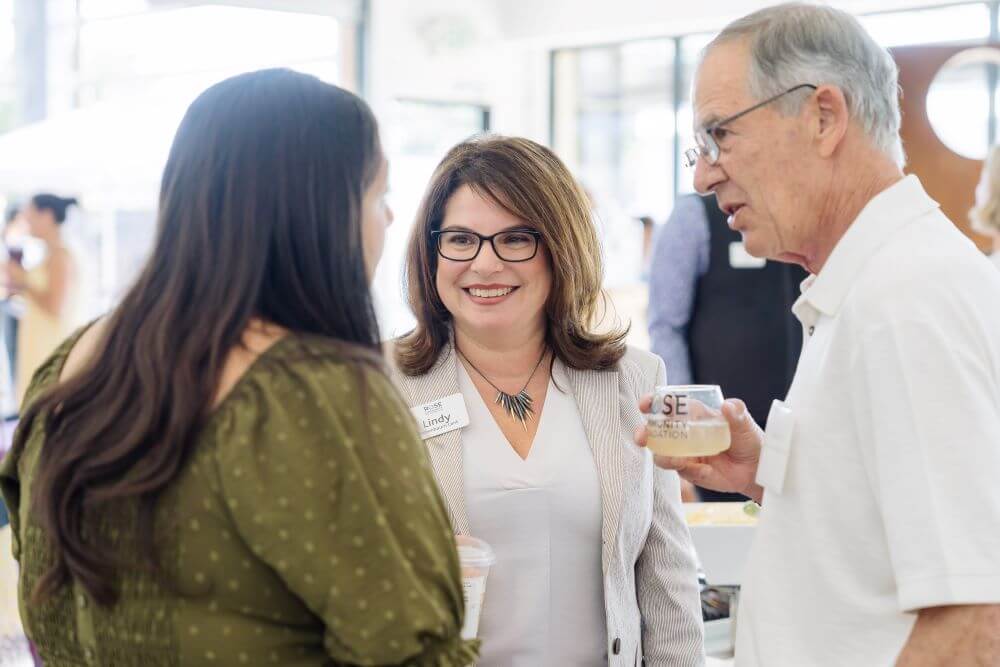 Two guests talking with President and CEO Lindy Eichenbaum Lent at the Rose Community Foundation Nonprofit Partners Celebration in August 2023